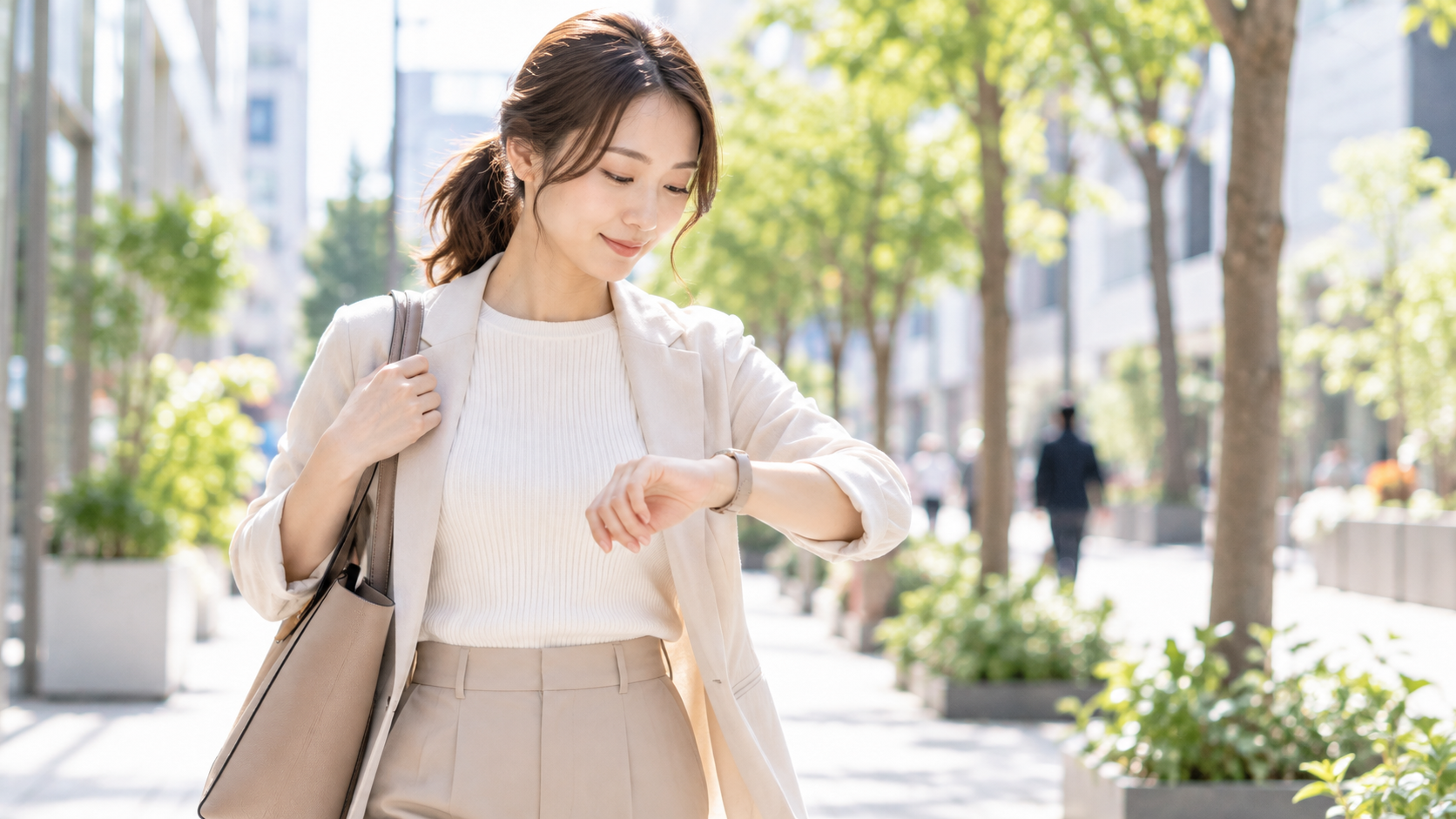 腕時計を見ながら並木道を歩く女性